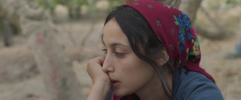 Movie still from “Under the Fig Trees” (2021), directed by Erige Sehiri – A woman with a red head scarf is holding her hand to her face; Close Up shot, Over the shoulder angle