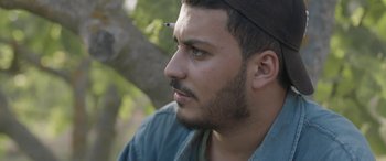Movie still from “Under the Fig Trees” (2021), directed by Erige Sehiri – A person wearing a hat; Close Up shot, Low angle