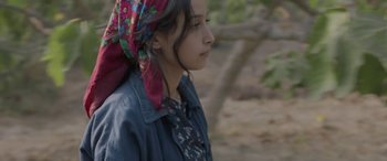 Movie still from “Under the Fig Trees” (2021), directed by Erige Sehiri – A young woman wearing a head scarf in a forest; Close Up shot, High angle