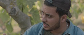 Movie still from “Under the Fig Trees” (2021), directed by Erige Sehiri – A person wearing a hat; Close Up shot, Over the shoulder angle