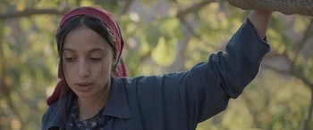 Movie still from “Under the Fig Trees” (2021), directed by Erige Sehiri – A young girl is holding her hand up to the sky; Close Up shot, Low angle