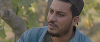 Movie still from “Under the Fig Trees” (2021), directed by Erige Sehiri – A person with a beard; Close Up shot, Over the shoulder angle