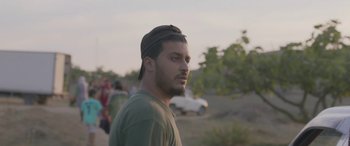 Movie still from “Under the Fig Trees” (2021), directed by Erige Sehiri – A man with a hat is standing in the grass; Close Up shot, Low angle