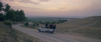 Movie still from “Under the Fig Trees” (2021), directed by Erige Sehiri – A group of people in the back of a white pickup truck; Extreme Wide shot, High angle