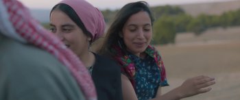 Movie still from “Under the Fig Trees” (2021), directed by Erige Sehiri – Two young women sitting on a bench in a field; Close Up shot, Low angle