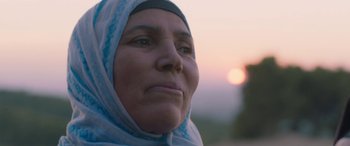 Movie still from “Under the Fig Trees” (2021), directed by Erige Sehiri – An older woman wearing a headscarf looking at the camera; Close Up shot, Low angle