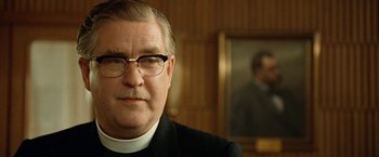 Movie still from “Under the Sun” (1998), directed by Colin Nutley – A man wearing glasses and a priest's outfit; Close Up shot, Low angle
