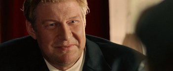 Movie still from “Under the Sun” (1998), directed by Colin Nutley – A person wearing a suit and tie; Close Up shot, Over the shoulder angle