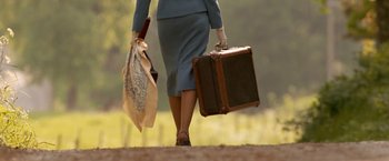 Movie still from “Under the Sun” (1998), directed by Colin Nutley – A woman in a blue suit carrying a suit case and umbrella; Wide shot, Low angle