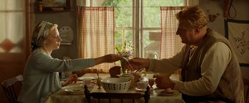 Movie still from “Under the Sun” (1998), directed by Colin Nutley – A group of people sitting at a table with a vase of flowers on it; Medium shot, High angle