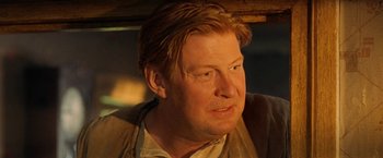 Movie still from “Under the Sun” (1998), directed by Colin Nutley – A person wearing a suit and tie; Close Up shot, Over the shoulder angle