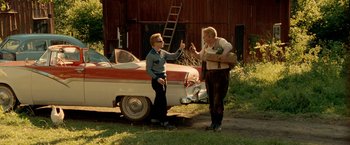 Movie still from “Under the Sun” (1998), directed by Colin Nutley – Two people standing in front of an old car; Wide shot, Over the shoulder angle