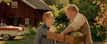 Movie still from “Under the Sun” (1998), directed by Colin Nutley – A man holding a box of vegetables next to another man; Medium shot, Over the shoulder angle