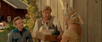 Movie still from “Under the Sun” (1998), directed by Colin Nutley – A man handing a box to a woman holding a bag; Medium shot, Over the shoulder angle