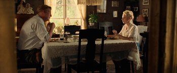 Movie still from “Under the Sun” (1998), directed by Colin Nutley – Two people are sitting at a dining room table; Wide shot, Over the shoulder angle