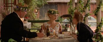 Movie still from “Under the Sun” (1998), directed by Colin Nutley – A woman sitting at a dinner table with a flower crown on her head; Medium shot, Over the shoulder angle