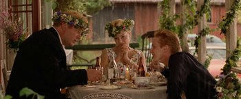 Movie still from “Under the Sun” (1998), directed by Colin Nutley – A group of people sitting at a table with food; Medium shot, Over the shoulder angle