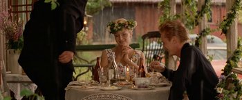 Movie still from “Under the Sun” (1998), directed by Colin Nutley – A woman sitting at a dinner table with wine bottles; Medium shot, Over the shoulder angle