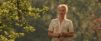 Movie still from “Under the Sun” (1998), directed by Colin Nutley – A woman holding a golf club while standing next to a tree; Medium shot, Over the shoulder angle