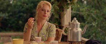 Movie still from “Under the Sun” (1998), directed by Colin Nutley – A woman sitting at a table holding a piece of cake; Medium shot, Over the shoulder angle