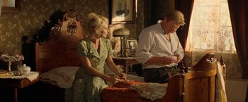 Movie still from “Under the Sun” (1998), directed by Colin Nutley – A man and a woman sitting on a bed in a room; Medium shot, Over the shoulder angle