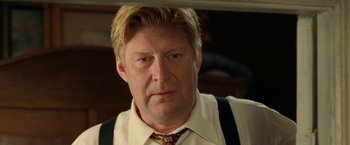 Movie still from “Under the Sun” (1998), directed by Colin Nutley – A person wearing a suit and tie; Close Up shot, Low angle