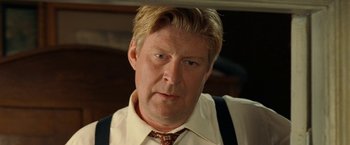 Movie still from “Under the Sun” (1998), directed by Colin Nutley – A person wearing a suit and tie; Close Up shot, Over the shoulder angle