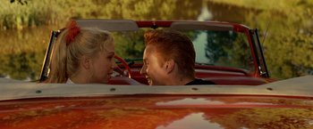 Movie still from “Under the Sun” (1998), directed by Colin Nutley – A man and a woman sitting in the back seat of a red car; Close Up shot, Over the shoulder angle