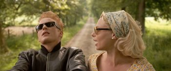 Movie still from “Under the Sun” (1998), directed by Colin Nutley – A man and a woman riding a motorcycle down a dirt road; Close Up shot, Low angle