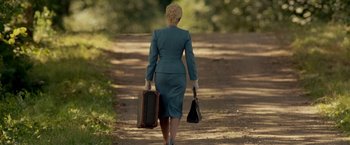 A woman walking down a dirt road carrying a suit case