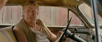Movie still from “Under the Sun” (1998), directed by Colin Nutley – A man sitting in the drivers seat of a car; Close Up shot, Low angle