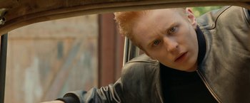 Movie still from “Under the Sun” (1998), directed by Colin Nutley – A person with blonde hair and a black leather jacket; Close Up shot, Low angle