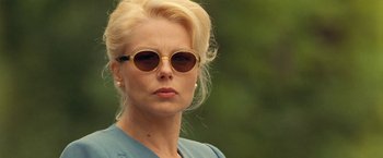Movie still from “Under the Sun” (1998), directed by Colin Nutley – A woman with blonde hair wearing sunglasses and a blue shirt; Close Up shot, Over the shoulder angle