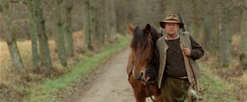 Movie still from “Under the Sun” (1998), directed by Colin Nutley – A man walking a horse down a dirt road; Medium shot, Low angle