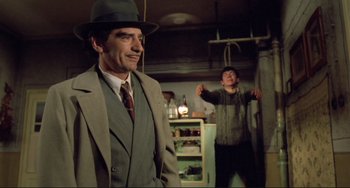 Movie still from “Underground” (1995), directed by Emir Kusturica – A man wearing a suit and a hat standing next to another man in a room; Medium shot, Over the shoulder angle