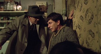 Movie still from “Underground” (1995), directed by Emir Kusturica – A man in a hat and a sweater is leaning against a wall while another man in a hat and a sweater is leaning against a wall; Medium shot, Low angle