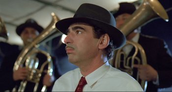 Movie still from “Underground” (1995), directed by Emir Kusturica – A man in a hat and a tie with other people in the background; Close Up shot, Low angle