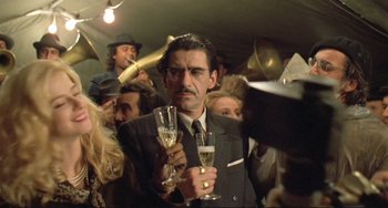 Movie still from “Underground” (1995), directed by Emir Kusturica – A man holding two champagne flutes in front of a crowd; Medium shot, Low angle