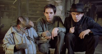 Movie still from “Underground” (1995), directed by Emir Kusturica – Two men sitting next to each other next to a chimpanzee; Medium shot, Low angle