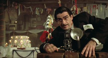 Movie still from “Underground” (1995), directed by Emir Kusturica – A man in a suit and tie holding a camera; Close Up shot, Low angle