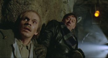 Movie still from “Underground” (1995), directed by Emir Kusturica – Two men are leaning against a rock wall; Medium shot, High angle