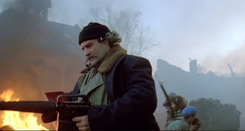 Movie still from “Underground” (1995), directed by Emir Kusturica – A man holding a gun while standing next to a tree; Medium shot, Low angle