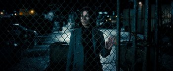 Movie still from “Underworld: Awakening” (2012), directed by Björn Stein – A woman standing behind a chain link fence at night; Medium shot, Over the shoulder angle
