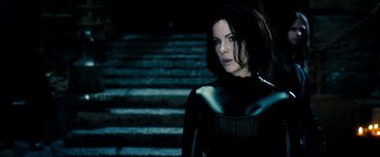 Movie still from “Underworld: Awakening” (2012), directed by Björn Stein – A woman in a black outfit standing in front of a set of stairs; Medium shot, Over the shoulder angle