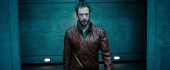 Movie still from “Underworld: Awakening” (2012), directed by Björn Stein – A man in a brown leather jacket standing in front of a blue wall; Medium shot, Low angle
