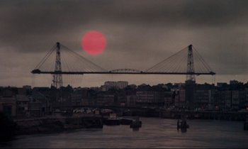 Movie still from “A Room in Town” (1982), directed by Jacques Demy – The sun is setting over a city with a bridge; Extreme Wide shot, High angle