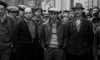 Movie still from “A Room in Town” (1982), directed by Jacques Demy – Black and white photograph of a group of men standing together; Medium shot, Low angle