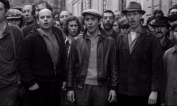 Movie still from “A Room in Town” (1982), directed by Jacques Demy – A black and white photo of a group of people; Medium shot, High angle