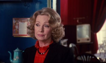 Movie still from “A Room in Town” (1982), directed by Jacques Demy – An older woman in a red blouse and black jacket; Close Up shot, Over the shoulder angle