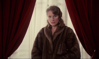 Movie still from “A Room in Town” (1982), directed by Jacques Demy – A woman in a fur coat standing in front of a window; Medium shot, Over the shoulder angle